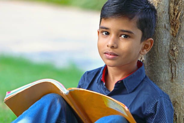 istock Little boy posing to camera,Sitting on green grass with school text book 1096769420