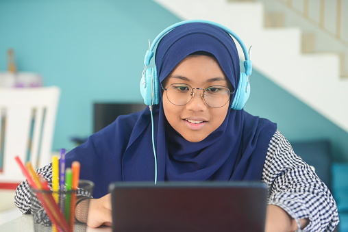 Asian teenage girl with headphones doing homework with digital tablet