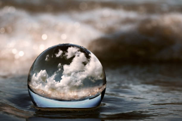 Summer clouds displayed through a transparent glass ball on the beach sand of a lake shore