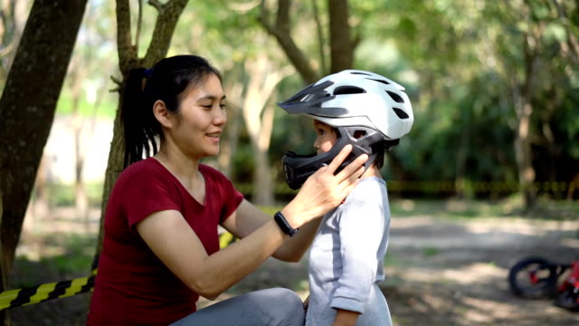 SLO MO Asian Mother is putting safety helmet on his little son's head.