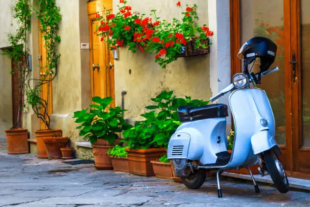 Gorgeous cute decorated street with flowers and rustic entrance, old fashioned scooter standing in typical Italian street, Pienza, Tuscany, Europe