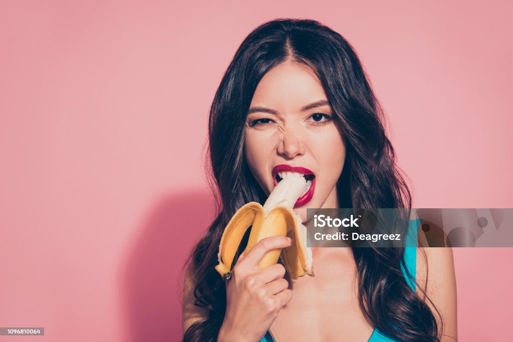 Close-up portrait of nice cheeky cunning adorable glamorous char Close-up portrait of nice cheeky cunning adorable glamorous charming attractive wavy-haired lady holding biting banana red lips isolated over pink pastel background Sensuality Stock Photo