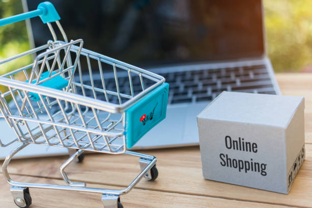 Cardboard box with symbol and trolley in front of laptop keyboard with natural green background. Consumer can buy product directly anywhere anytime from seller. Online shopping and e-commerce concept. caja de cartón con símbolo y carretilla delante de teclado del ordenador portátil con fondo verde natural. consumidor puede comprar producto directamente en cualquier lugar en cualquier momento al vendedor. concepto de compras y de comercio electrónico
