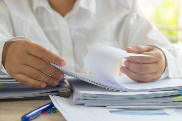 istock Teacher open paper by hand for checking student homework assignments on desk in school office. Unfinished paperwork stacked in archive with color binder paper clips. Education and business concept. 1096812488