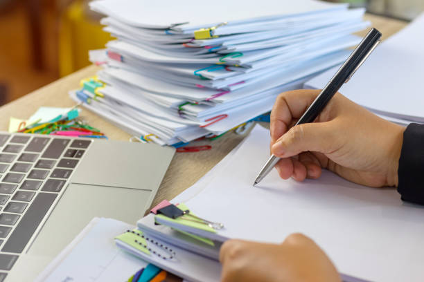 istock Teacher holding pen by hand for checking student homework assignments on desk in school office. Unfinished paperwork stacked in archive with color binder paper clips. Education and business concept. 1096813076