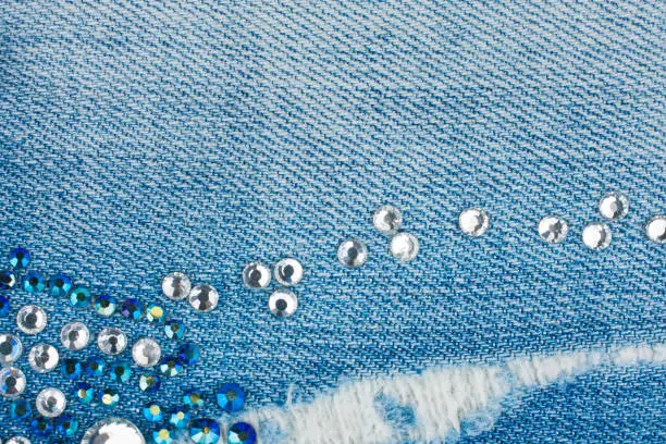 Light-blue torn denim with blue and silver rhinestones, background. Top view