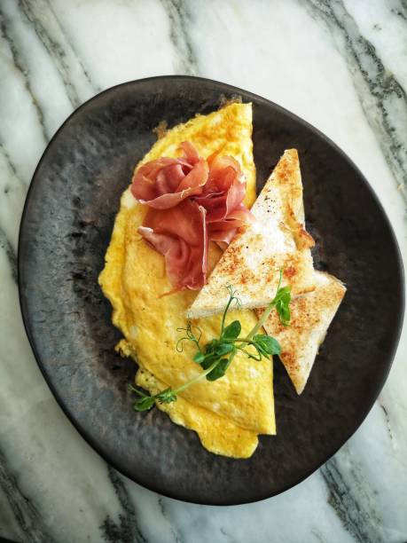 A fresh omelette topped with parma ham and toast on a marble table
