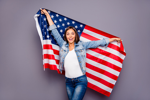 Cute sweet lovely excited smiling lady emigrant worker  holding USA american flag behind back, isolated over grey background