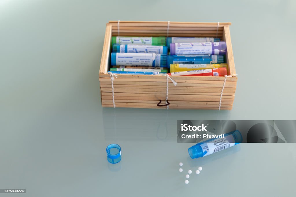 Homeopathic globules scattered around with their colored containers in the shape of tube Homeopathic Medicine Stock Photo