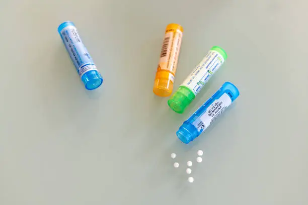 Homeopathic globules scattered around with their colored containers in the shape of tube