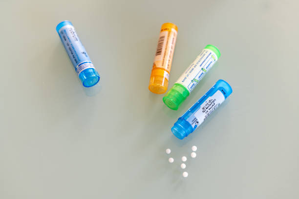 homeopathic globules scattered around with their colored containers in the shape of tube - homeopatic medicine imagens e fotografias de stock