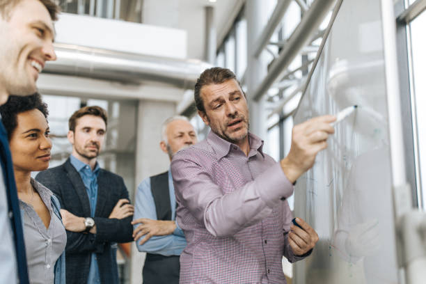 istock Mid adult entrepreneur talking while drawing business development on whiteboard. 1096834884