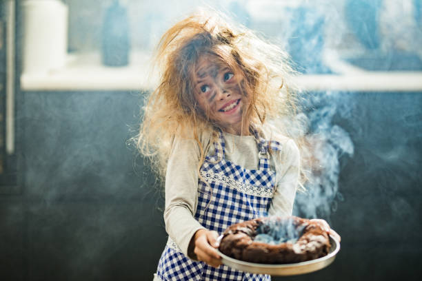 Whops, I have burnt the cake! Happy little girl with messy hair holding burnt the cake in the kitchen. chaos stock pictures, royalty-free photos & images