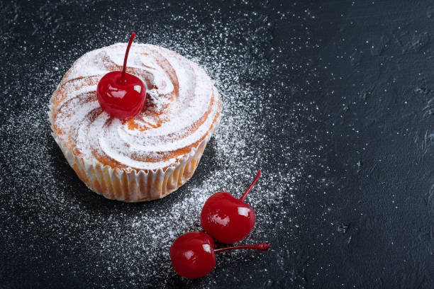 Muffin in powdered sugar with cherries over black texture background.
