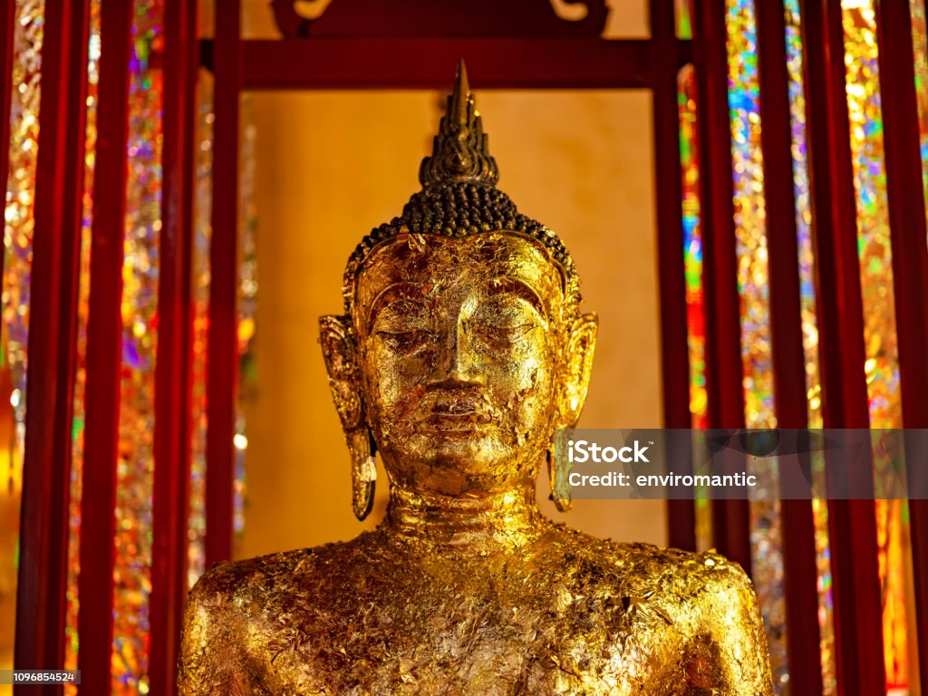 Statue of a Buddha image covered in gold leaf in the grounds of a typical Thai Buddhist temple. Statue of a Buddha image covered in gold leaf in the grounds of a typical Thai Buddhist temple. Selective focus with focus on the eyes. Abstract Stock Photo