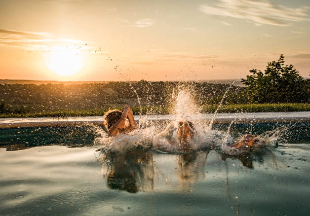Jumping into the pool at sunset! Carefree parent and his kids jumping in the pool at sunset. jumping into water stock pictures, royalty-free photos & images
