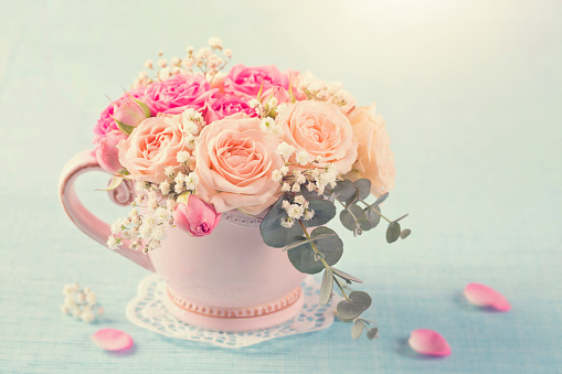 Pink roses in a teacup on a pastel blue background