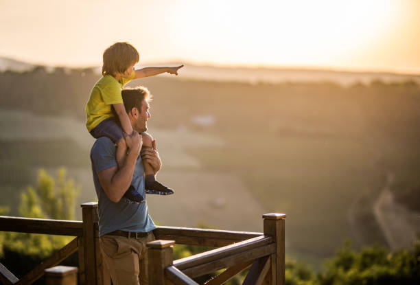 Daddy, look over there! Happy single father carrying his son on shoulders at the balcony while boy is aiming at distance. Copy space. on shoulders stock pictures, royalty-free photos & images