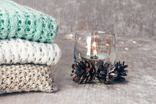 istock Stylish knitted pastel colored sweaters folded in stack with pine cones and candle on velvety fabric background. Winter and spring season knitwear clothing. Close up, copy space. 1096872254
