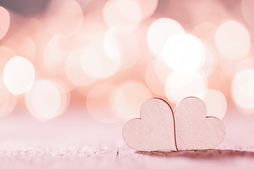 Two small handmade pink wooden hearts on bright lights bokeh background