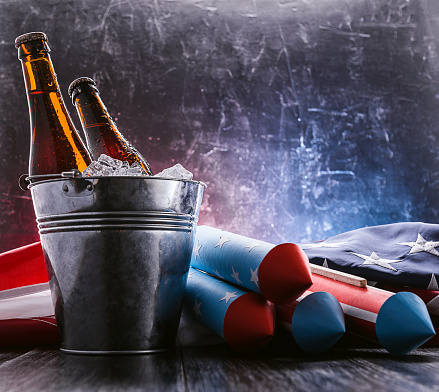 two bottles of beer in an ice bucket with the American flag lying nearby and rockets for fireworks. Independence Day celebration concept