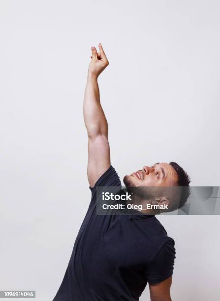 Grab Gesture Or Climb Something Portrait Of Casual Man Wearing A Darck Shirt Stretches His Hand Up Ase Wants To Get Something Or He Wants To Screw In A Light Bulb On Grey Background Stock Photo - Download Image Now