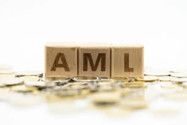 Money laundering concept, wooden word block "AML" on plie of coins.