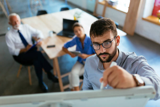 mid adult businessman writing a business plan on whiteboard during a meeting at conference room - writing whiteboard men businessman imagens e fotografias de stock