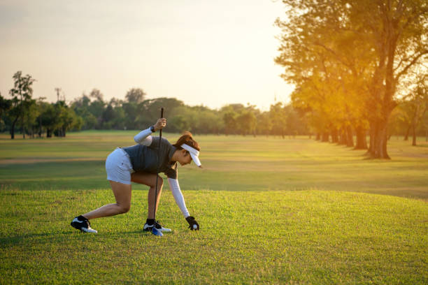 sportliche golfer asiatische frau aufstellen golfball auf tee mit club golfplatz an sonnigen tag für gesunden sport. lifestyle und sport-konzept - golf power golf course challenge stock-fotos und bilder