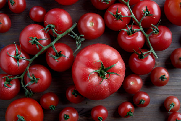 istock Perfect fresh differetn sort red tomatoes on a branch at wooden background from above. 1096960200