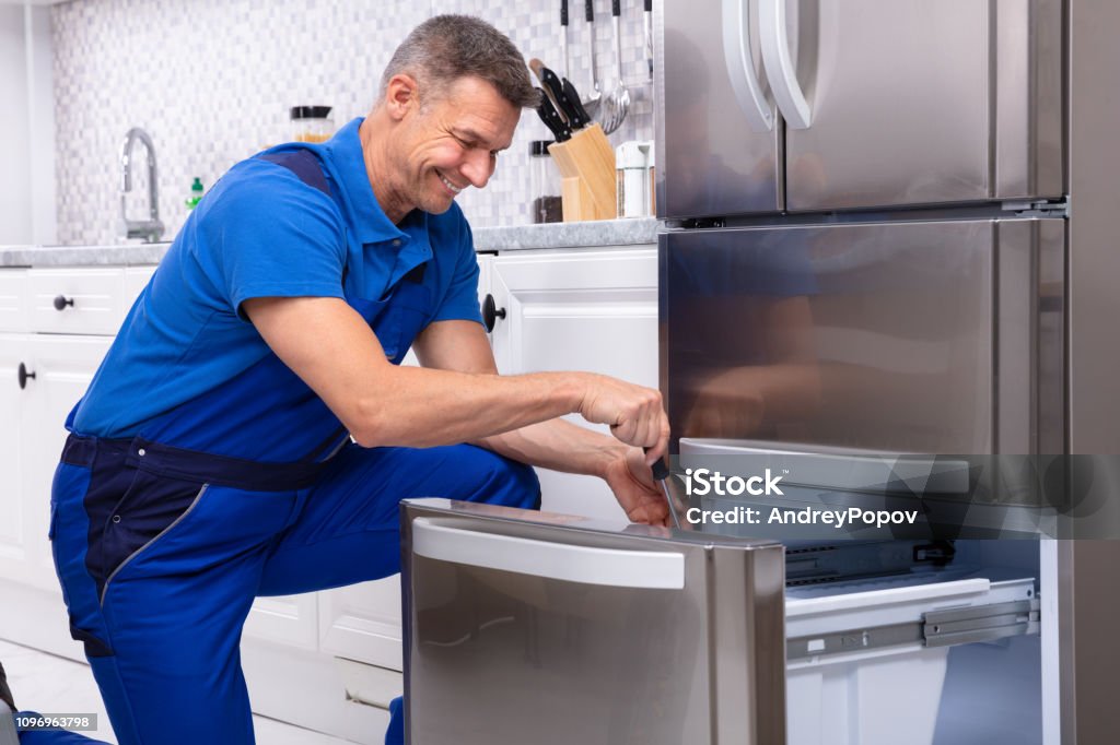 Serviceman Repairing Refrigerator Mature Male Serviceman Repairing Refrigerator With Toolbox In  Kitchen Repairing Stock Photo