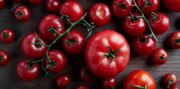 istock Perfect fresh differetn sort red tomatoes on a branch at wooden background from above. 1096964270