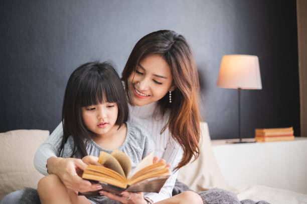 szczęśliwa azjatycka matka rodziny i córka na łóżku w sypialni mówią dobrą noc przed snem - child reading mother book zdjęcia i obrazy z banku zdjęć