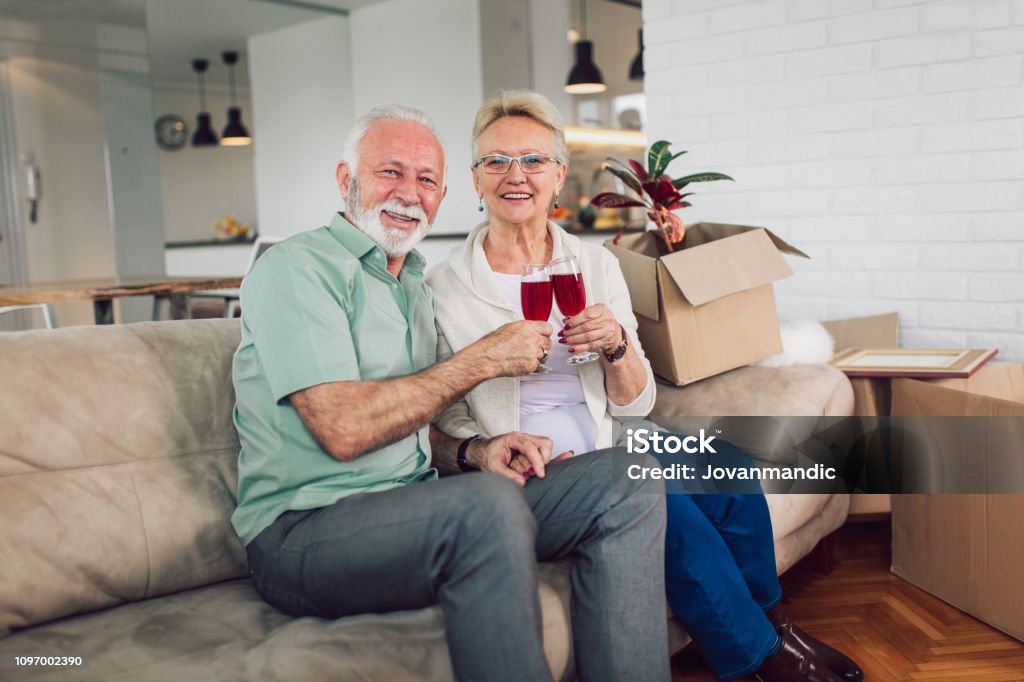 陽気な年配のカップルは、お互いでワインを飲む新しいホーム笑顔に移動します。 - シニア世代のロイヤリティフリーストックフォト