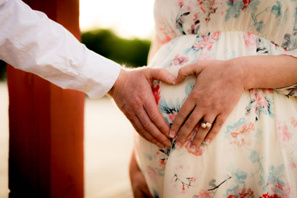 istock Expecting father with hand on mothers belly forming a heart 1097004522
