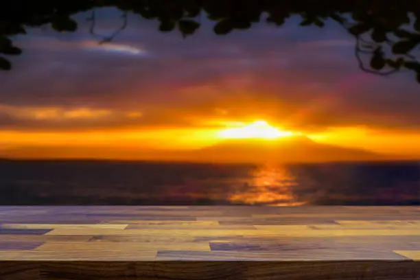 Photo of Empty table top with tropical paradise island and sunset and ocean blurred in the background.