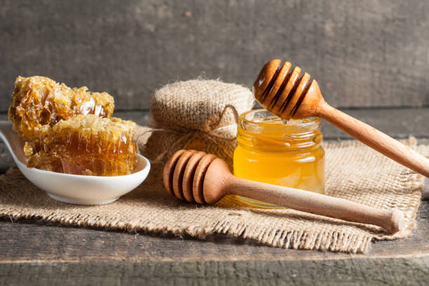 miele gocciolante da un cenato di miele di legno in un barattolo su sfondo rustico grigio legno - honey purity raw pollination foto e immagini stock
