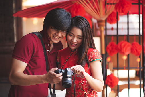 Happy Asian Chinese Couple Wearing Cheongsam Traditional Red Dress and T-Shirt and Looking on Camera in Travel Trip on Chinese New Year Holiday