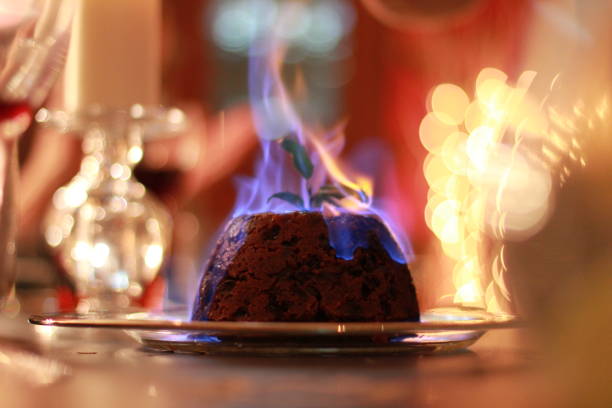 Burning Christmas Pudding Burning Christmas pudding with a tall, single blue flame. Background of glasses, lights, and table, is blurred and out of focus. Landscape orientation. christmas pudding stock pictures, royalty-free photos & images