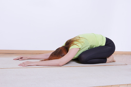 Caucasian white female yoga master working yoga exercise. Pose: \nPolar bear (BALASANA)\nstretches the spine, opens the hips, massages the tops of the feet, turns the mind inwards, promotes optimal fetal health in pregnancy\nShot in apartment yoga studio.