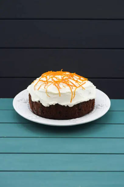 Minimalist style pastry. Homemade traditional fruit cake with cream icing and orange peel on blue background copyspace vertical
