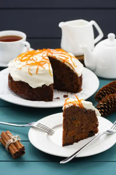 Homemade chocolate fruit cake with cream cheese icing and orange peel served with black tea on blue background vertical