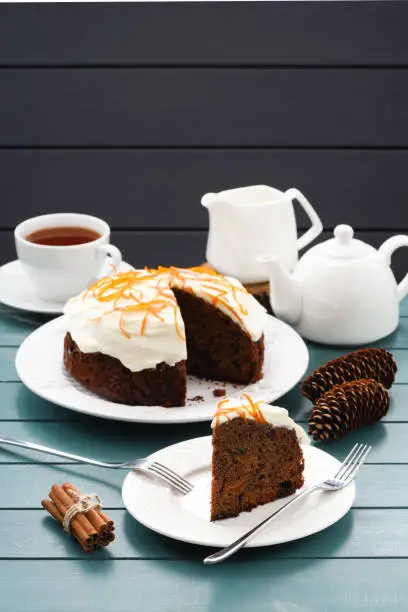Hygge tea party. Black tea and traditional fruit cake with cream icing and orange peel on blue background copyspace