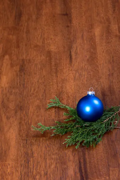 A blue christmas ornament ball with a piece of evergreen greenery on a wooden surface