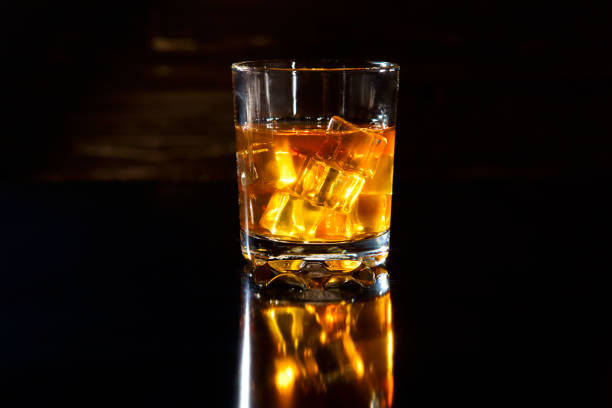 Glass of whiskey with ice cubes on a black table