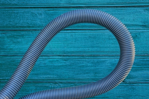 one long gray plastic hose against a green wooden wall