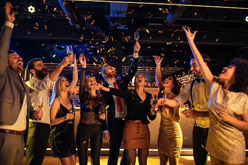 Happy young friends enjoying drinks while dancing on dance floor in nightclub