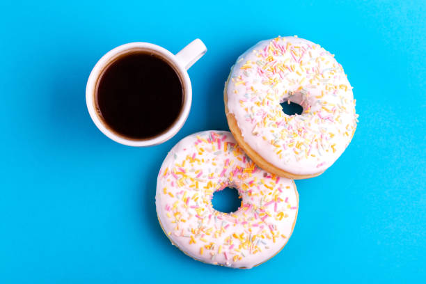 istock Two delicious vanilla donuts with sprinkle and cup of coffee on bright blue background 1097126354