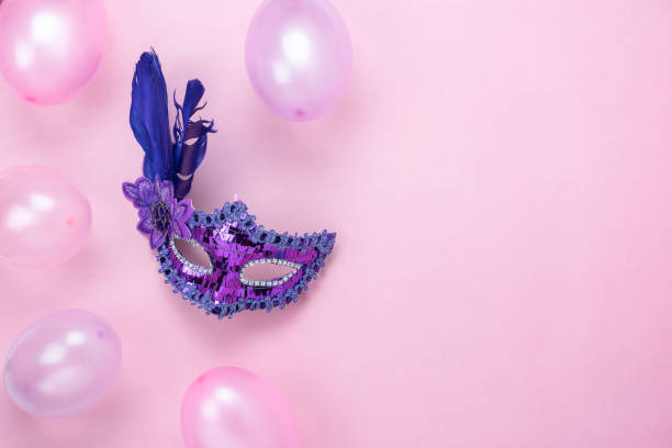 Table top view aerial image of beautiful colorful decorations Mardi Gras or carnival festival background.Flat lay accessory objects the mask & decor purple & pink balloon on modern pink paper. stock photo