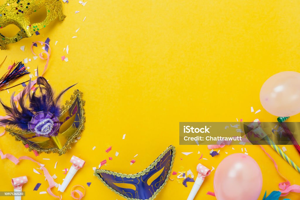 Table top view aerial image of beautiful colorful decorations carnival festival background.Flat lay accessory object the mask & decor confetti and pink balloon on modern yellow paper.copy space. Carnival - Celebration Event Stock Photo